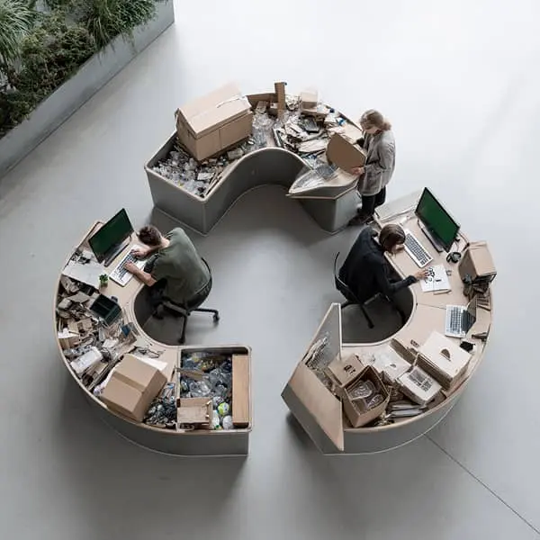 Postes de travail en forme de symbole du recyclage, avec écrans affichant des données et collaborateurs triant des matériaux, illustrant la RSE, l’économie circulaire et le pilotage durable par la data.