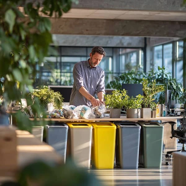 Employé de bureau triant des déchets dans des bacs de recyclage colorés, illustrant une démarche écoresponsable en entreprise.