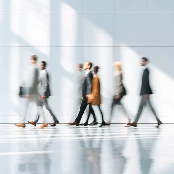 Groupe de professionnels en mouvement flou marchant dans un couloir lumineux, symbolisant la dynamique et le rythme du monde du travail moderne.
