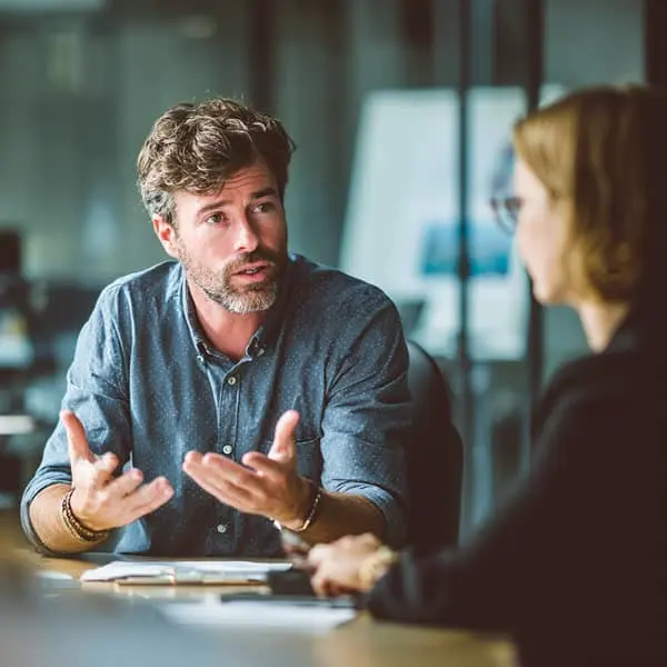 Homme en réunion expliquant un point à une collègue dans un bureau moderne, illustrant la communication professionnelle.