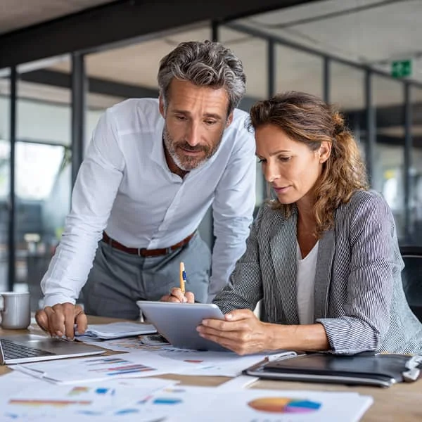 Deux collègues analysant des graphiques et des données sur une tablette et des documents, illustrant la collaboration et la prise de décision en entreprise.