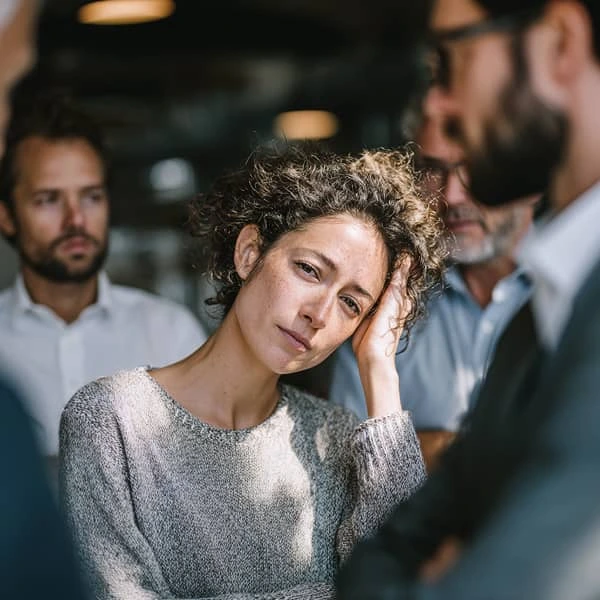 Femme semblant fatiguée ou stressée tenant sa tête dans un environnement de travail, entourée de collègues inquiets.