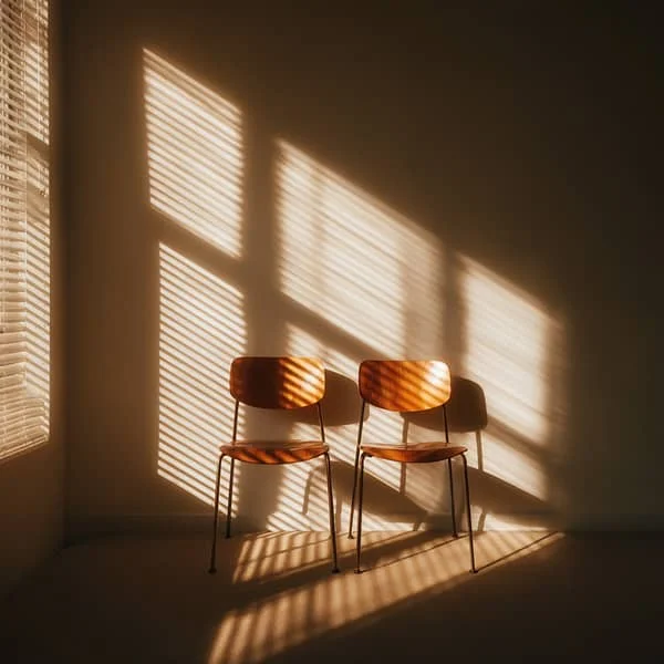 Deux chaises en bois placées côte à côte dans une pièce ensoleillée, symbolisant l’attente ou la rencontre professionnelle.
