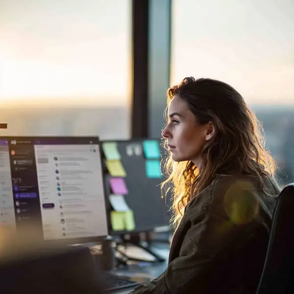 Responsable RH concentrée devant son écran d’ordinateur, au coucher du soleil, dans un open space moderne avec des post-it colorés sur les écrans.