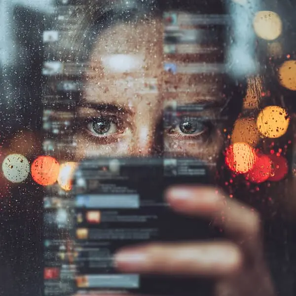 Gros plan sur le regard d’une personne observant son smartphone sous la pluie, avec des notifications floues en surimpression, illustrant la pression d’un bad buzz et la gestion d’une crise de réputation en ligne.
