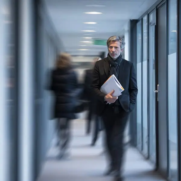 Professionnel des ressources humaines marchant dans un couloir de bureaux modernes, des dossiers sous le bras, illustrant les enjeux administratifs et juridiques liés aux évolutions sociales en entreprise.