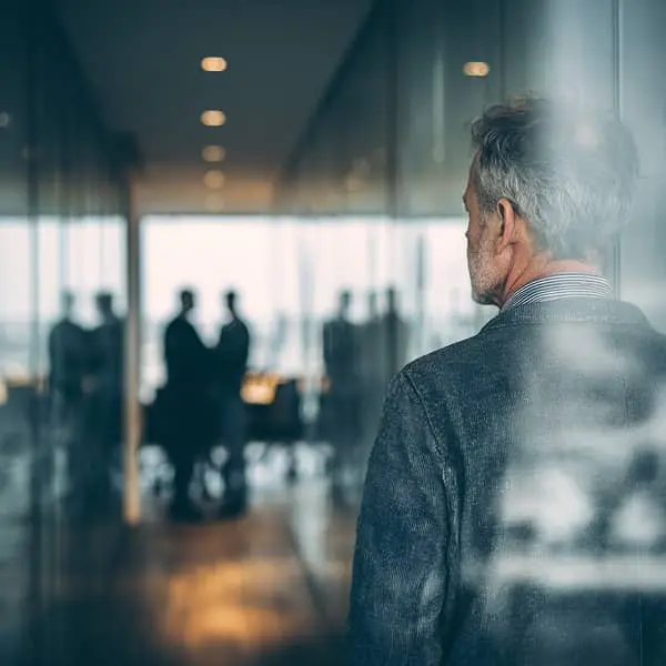 Salarié senior observant une réunion à travers une paroi vitrée, illustrant les freins liés à l’âge en entreprise