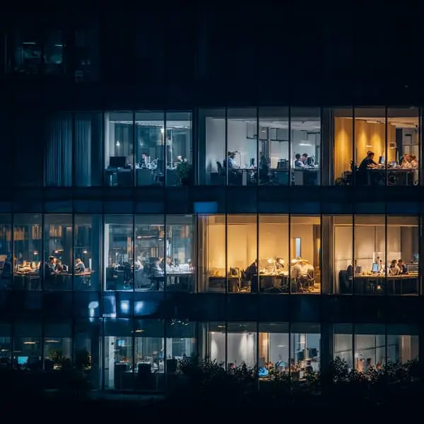 Bureaux d’entreprise éclairés la nuit avec des salariés travaillant en équipe, illustrant le travail de nuit