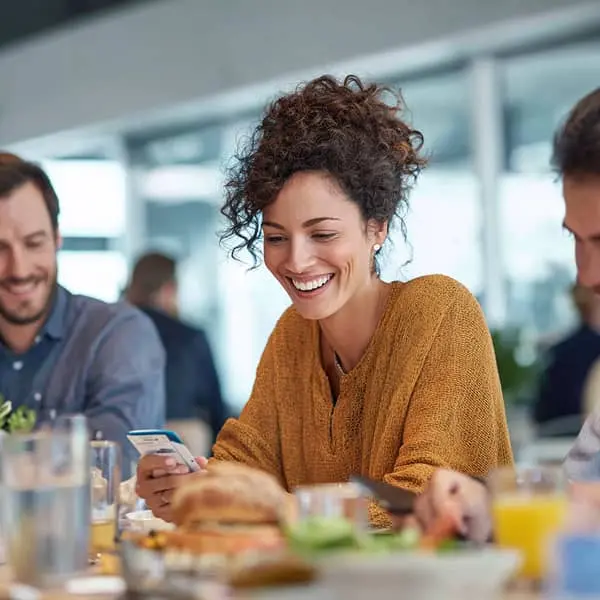 Salariée souriante utilisant une carte ou application de ticket restaurant lors d’un déjeuner entre collègues en entreprise
