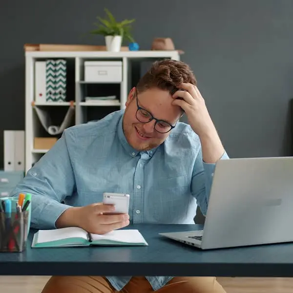 Salarié consultant son téléphone portable au bureau devant un ordinateur portable